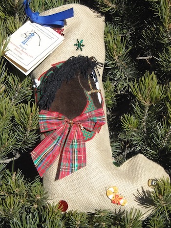 A Christmas stocking made of burlap. It has a brown horse surrounded by a wreath and a bow