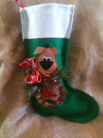 A green felt stocking with a white cuff, a cute brown dog in a wreath of pine cones and a bow