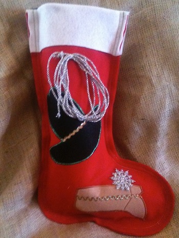 A red felt stocking with a white cuff decorated with a cowboy hat, a silver lariat, and a boot